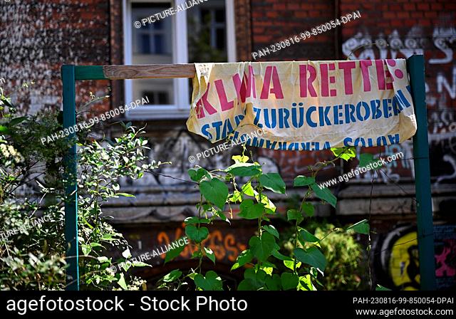 15 August 2023, Berlin: An old banner reads ""Climate, save, reclaim the city!"". Parking spaces for cars are being converted into green spaces and bicycle...