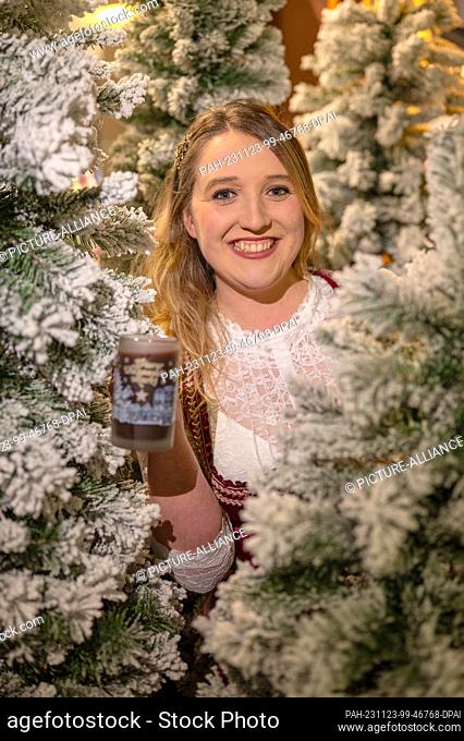 21 November 2023, Rhineland-Palatinate, Trier: The new German mulled wine queen Louisa Kress holds a mulled wine in the middle of artificial Christmas trees