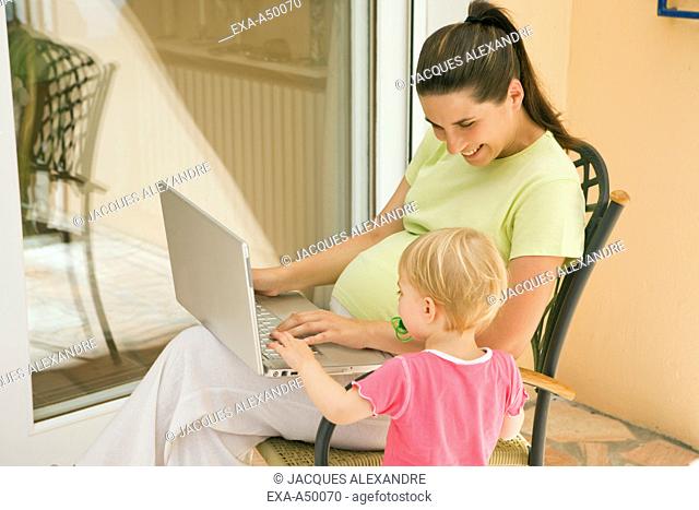 Pregnant mother showing her little girl the notebook on the terrace