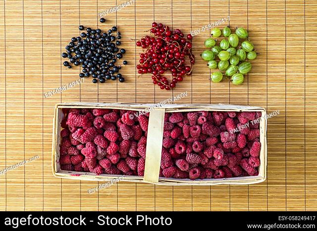 Fresh berries: Raspberry in the basket, gooseberries, currants, red currant on a bamboo mat. Flat lay, top view