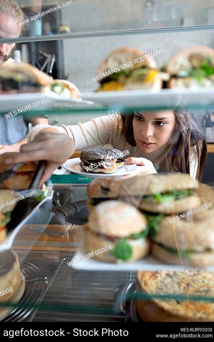 Barista taking burgers from display counter in cafe