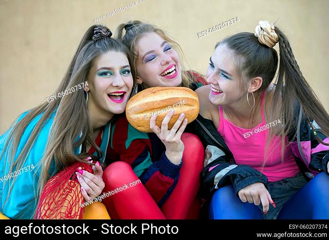 Three pretty girls dressed in the style of the nineties are sitting on the steps and sharing a roll