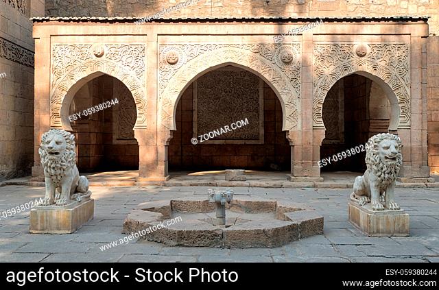 Two white marble lions statues and decorative fountain in front of three adjacent decorated stone arches at the garden of Manial Palace of Prince Mohammed Ali...