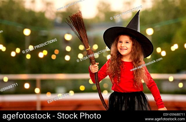 girl in black witch hat with broom on halloween