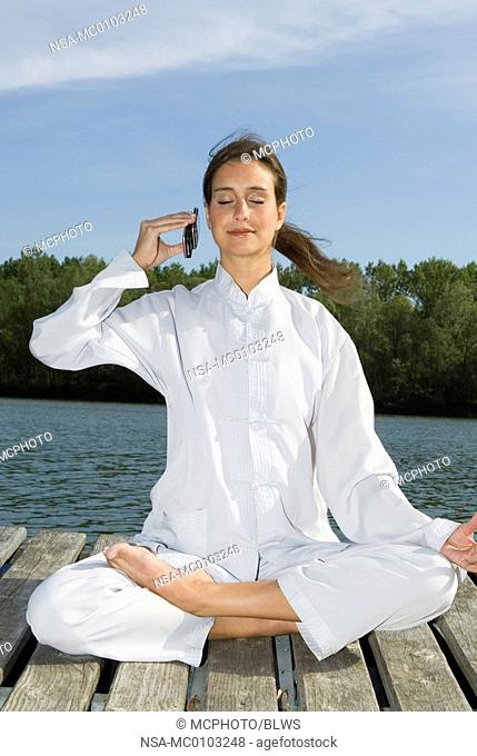 Woman practising Yoga, half lotus pose, Ardha Padmasana, Mudra and phoning