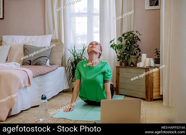 Woman practicing yoga e-learning through laptop at home