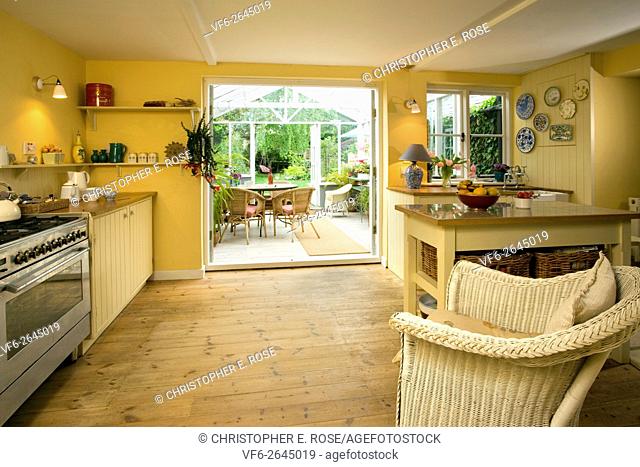 Exposed floor boards and cane furniture in a kitchen with conservatory attached. Editorial Use Only