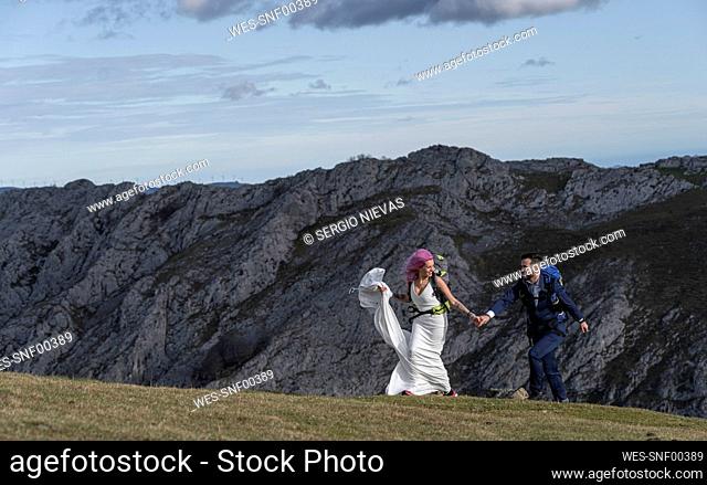 Bridal couple with climbing backpacks walking on meadow