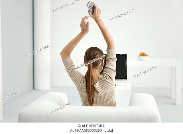 Woman watching TV with arms raised in air, rear view