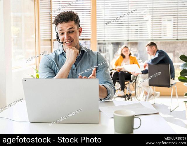 Young man with headset and laptop at desk in office