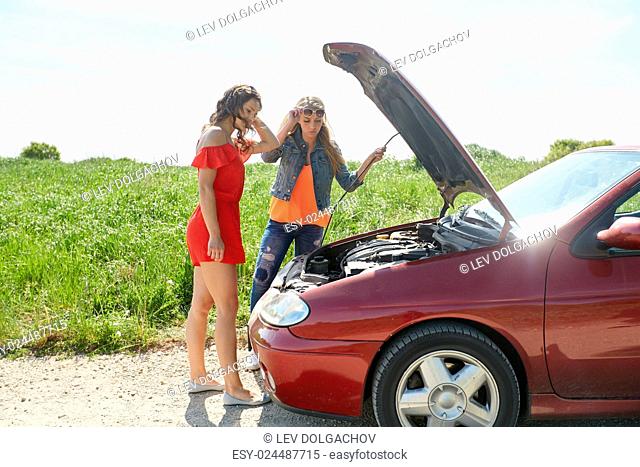road trip, transport, travel and people concept - young women with open hood of broken car at countryside
