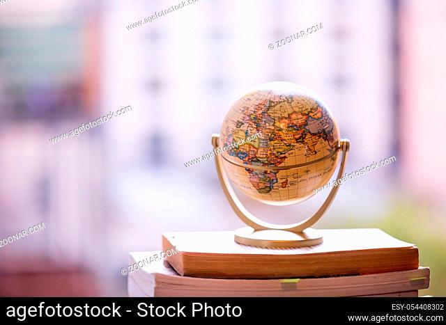 Miniature globe model standing on a stack of books. Symbol for travelling