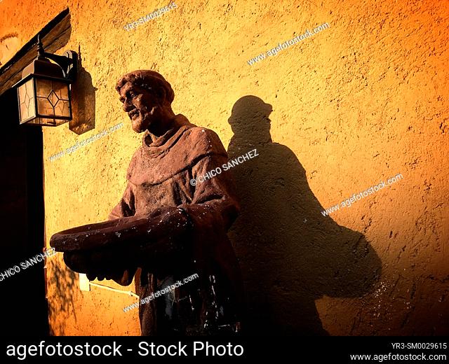 A sculpture of Saint Francis of Assisi decorates a chappel with an orange wall in Hostal Medieval in Peña de Bernal, Queretaro, Mexico