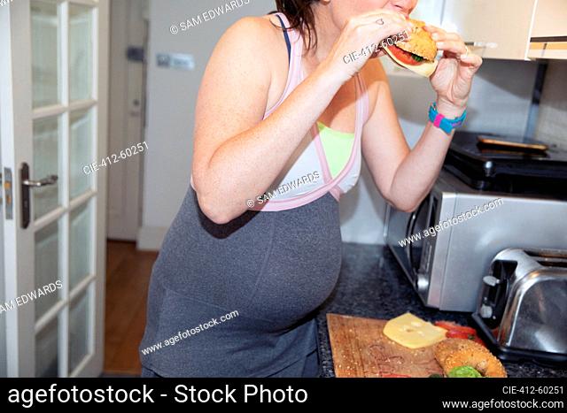 Pregnant woman eating sandwich in kitchen at home