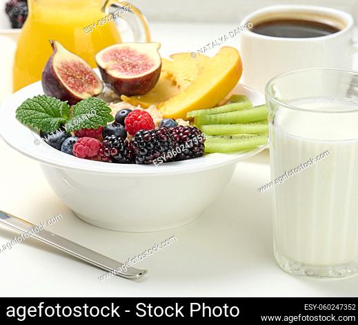 full plate with oatmeal and fruit, freshly squeezed juice in a transparent glass decanter, cup of coffee on a white table. Healthy breakfast