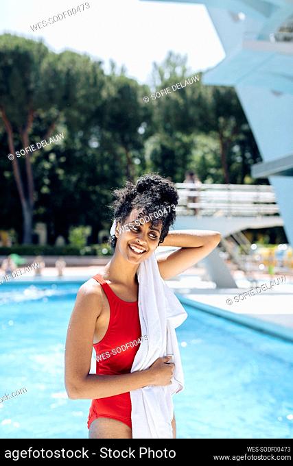 Portrait of smiling young woman in red bathsuit toweling in front of a pool