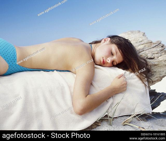Young woman sunbathing on large driftwook log at beach