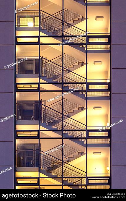 empty stairwell with staircase illuminated inside modern housing block viewed from outside through glasswall
