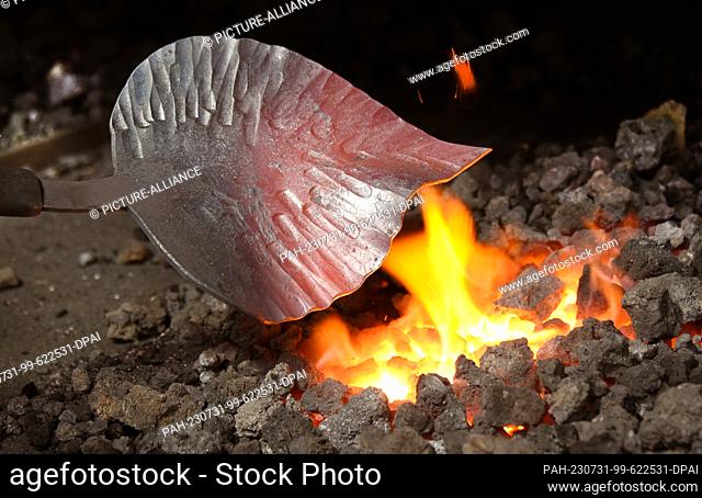 27 July 2023, Saxony, Hohenprießnitz: 39-year-old blacksmith and metal designer Marika Widdermann prepares a linden leaf for a fruit bowl in the forge of her...