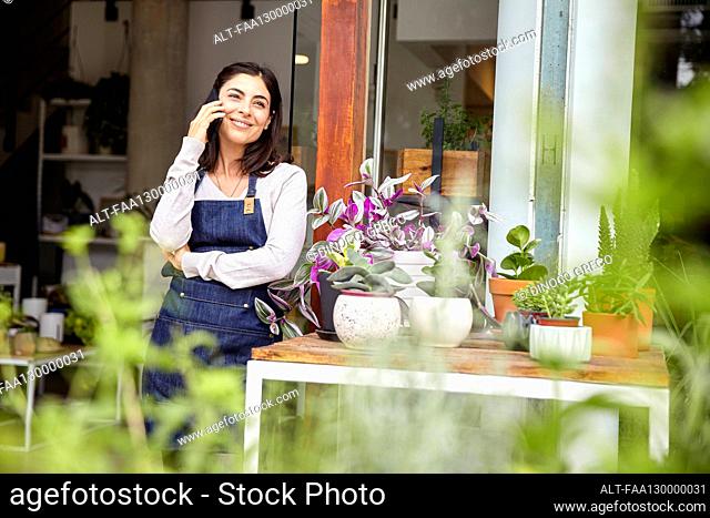 Young adult female entrepreneur talking on smartphone while standing in nursery