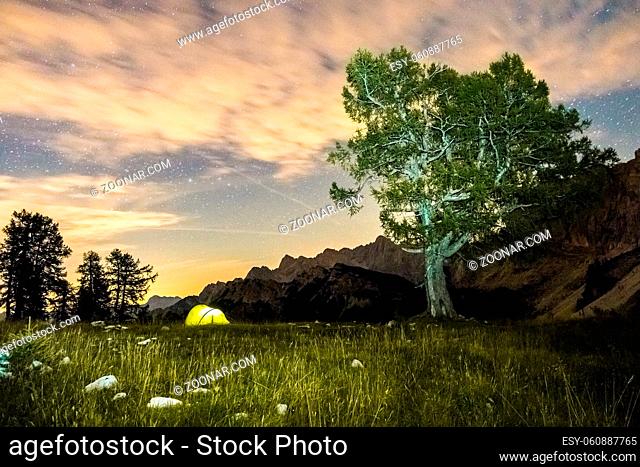 Illuminated camping tent at night. High altitude alpine landscape. Shining Stars in dark blue sky with purple clouds. Triglav National Park, Mountain Slemenova
