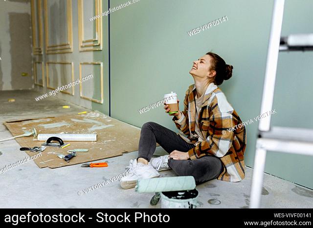 Young woman with disposable coffee cup laughing in apartment