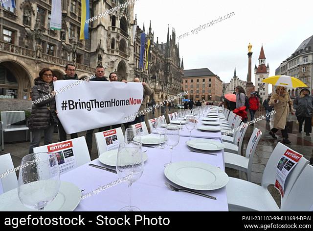 03 November 2023, Bavaria, Munich: The organizers of the campaign stand with a banner reading ""#BringThemHomeNow"" behind a blank Shabbat board with pictures...