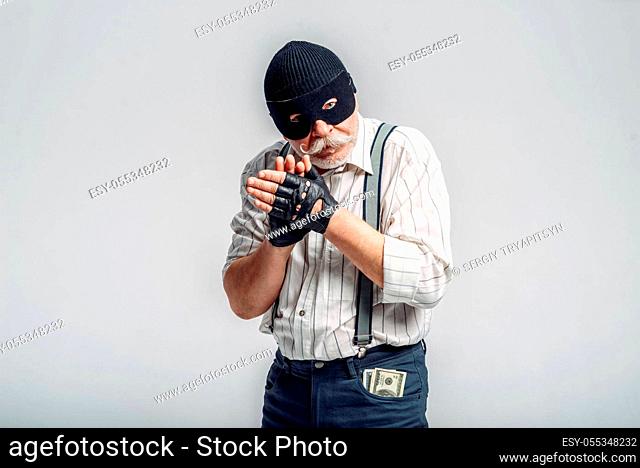 Elderly robber in mask isolated on grey background, gangster. Mature senior in studio, man in old age