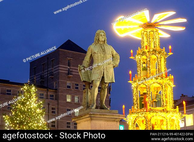 15 December 2021, Saxony-Anhalt, Halle: A pyramid of the so-called winter market lights up at the Händel monument with the town hall in the background