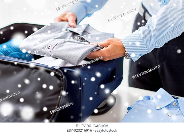 business, trip, luggage and people concept - happy businessman packing clothes into travel bag over snow effect