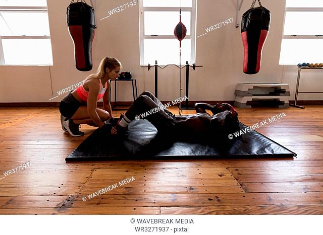 Trainer assisting male boxer in doing crunches in fitness studio