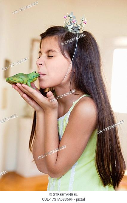 girl wearing crown kissing toy frog