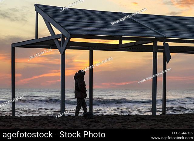 RUSSIA, REPUBLIC OF CRIMEA - DECEMBER 3, 2023: A person is seen on a beach in the city of Yevpatoria on Crimea's Black Sea coast at sunset in winter