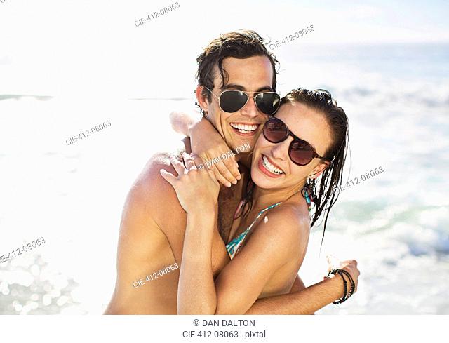 Portrait of enthusiastic couple in sunglasses hugging on beach