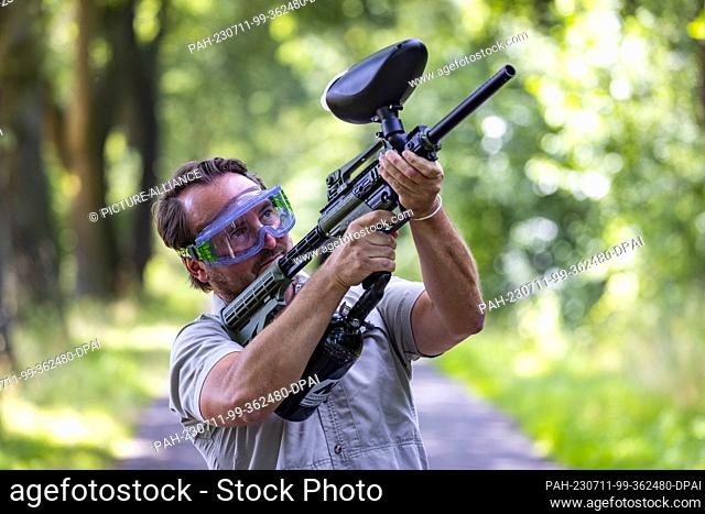 11 July 2023, North Rhine-Westphalia, Saerbeck: Ole Theisinger, a research assistant at Wald und Holz NRW, aims his paintball rifle at a web of oak...