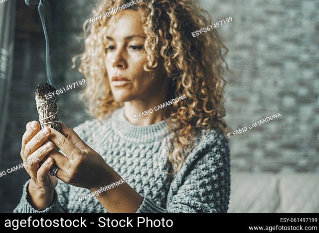 Portrait of a woman using a palo santo herbal incense to purify air and for spiritual leisure activity at home. Female people purify indoor house smoke burning...