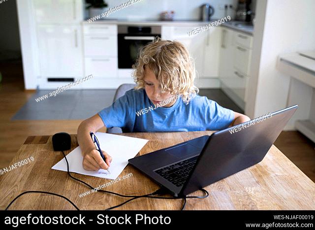 Boy doing homework with laptop on table at home