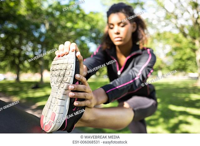 Pretty sporty woman stretching her leg in park