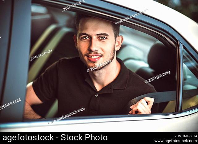 Young, handsome man fastens a seat belt, sitting in the back seat of the car
