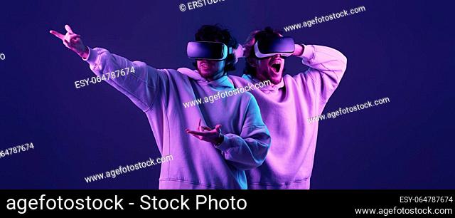 man in sweatshirt using virtual reality glasses on blue background. Neon lighting