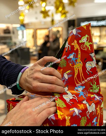 PRODUCTION - 09 December 2023, Baden-Württemberg, Ulm: A sales clerk wraps a Christmas present for customers in a department store