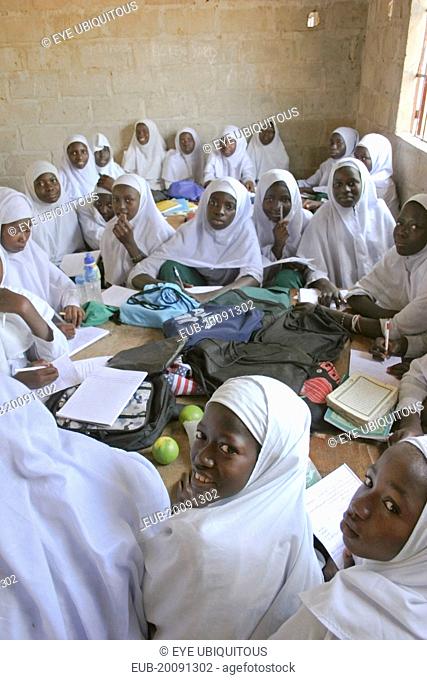 Tanji Village. African Muslim girls wearing white headscarves while attending a class at the Ousman Bun Afan Islamic school sitting in groups around desks with...