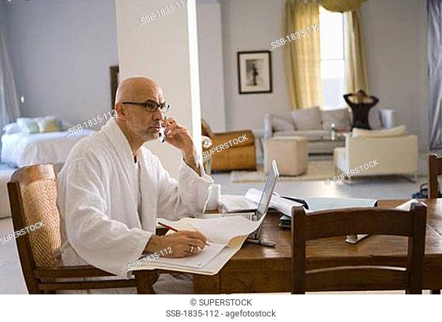 Side profile of a mature man talking on a mobile phone and writing with a pencil in a file