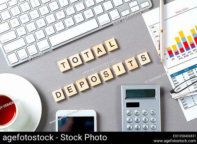 Total deposits concept with letters on wooden cubes. Still life of office workplace with supplies. Flat lay grey surface with keyboard and smartphone and cup of...