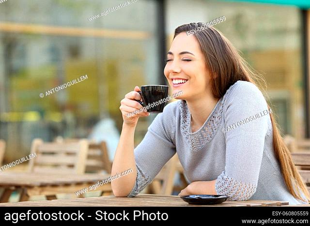 Satisfied happy woman smelling her cup of coffee sitting on a cafe terrace