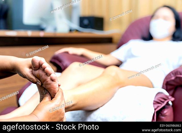 Close up asian woman do foot massage at home with face mask while city lockdown for social distance due to coronavirus pandemic