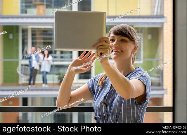 Portrait of smiling young woman using digital tablet for video chat with her neighbours