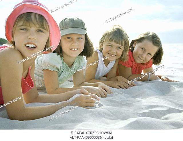Four girls lying on beach, smiling at camera, close-up