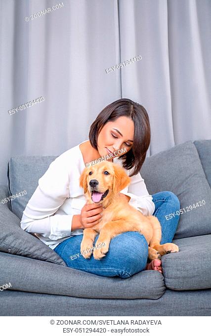 Indoor portrait of young woman sitting on sofa with her dog