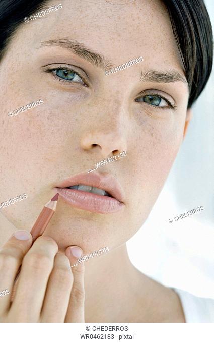 Portrait of a young woman applying lip liner on her lips
